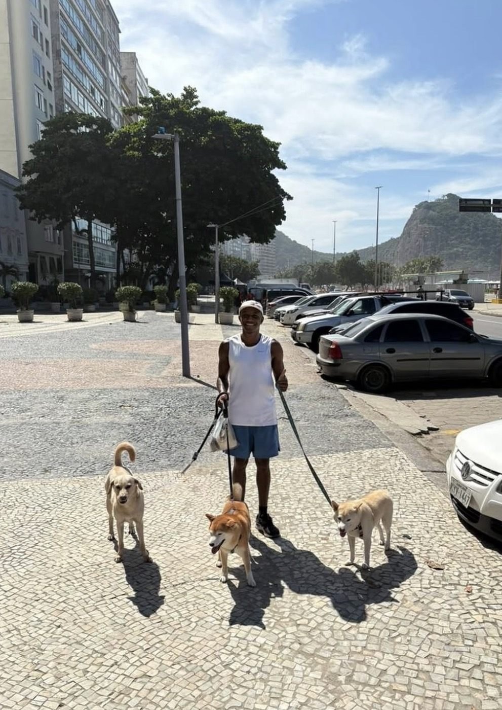 Breno sorrindo enquanto passeia com três cães no calçadão do Leme, no Rio de Janeiro